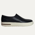 Black slip-on shoe with a white sole on a white background