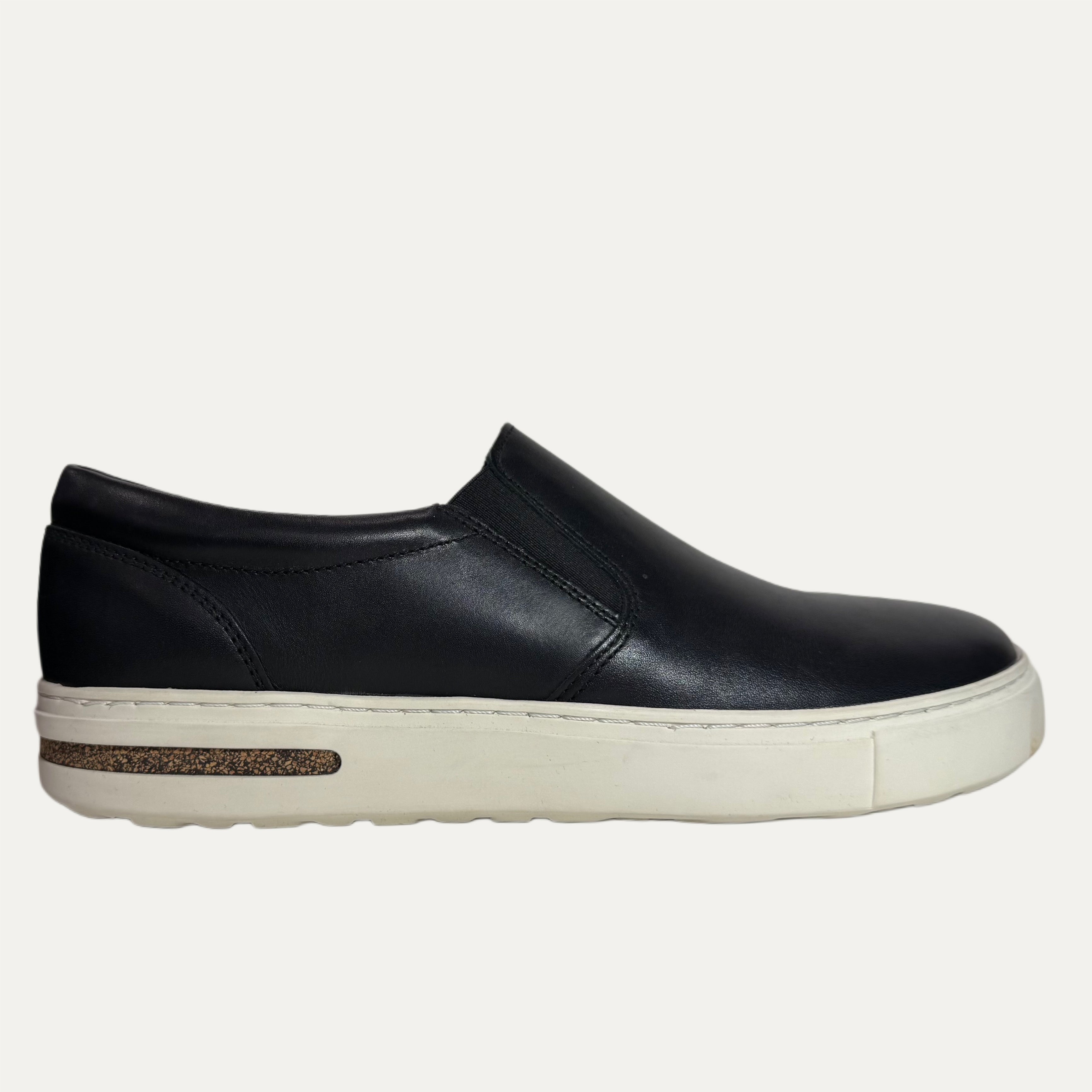 Black slip-on shoe with a white sole on a white background