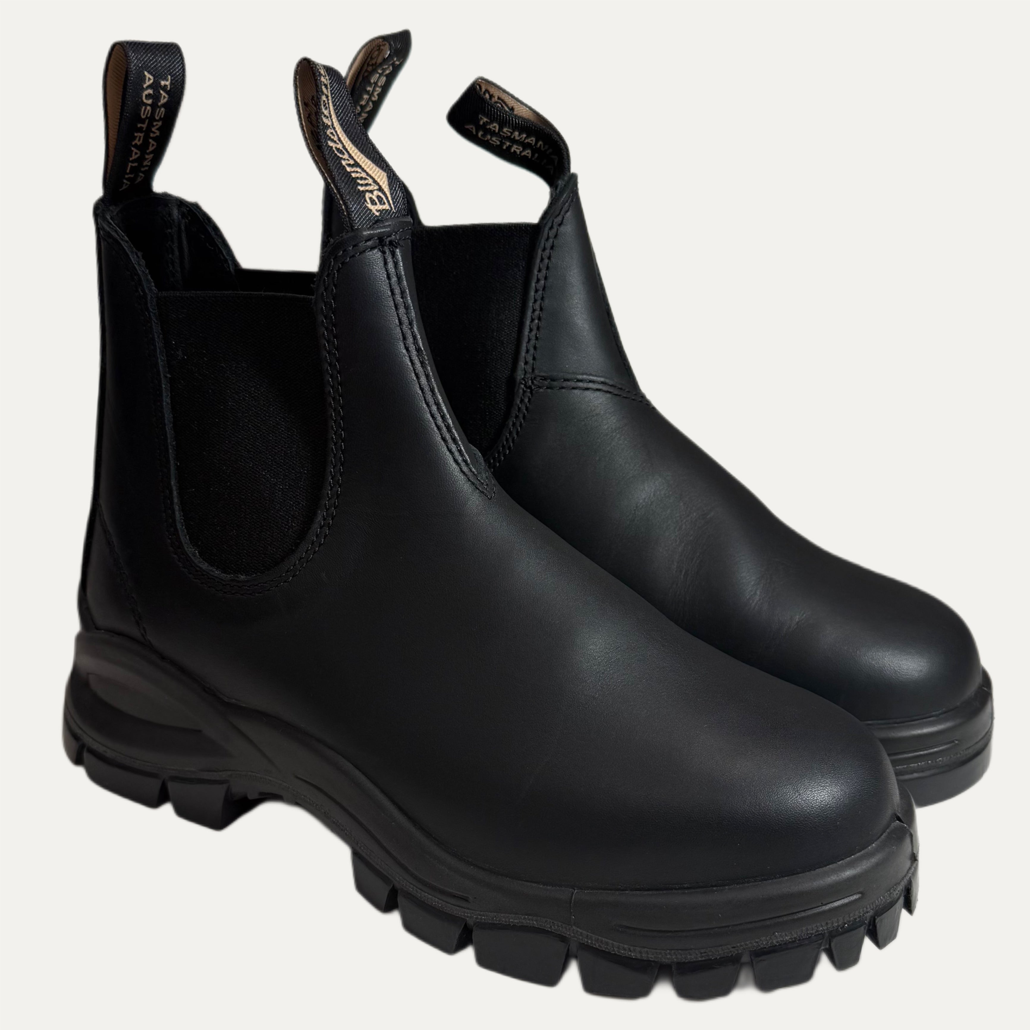 Pair of black lugged leather boots with thick soles on a light gray background