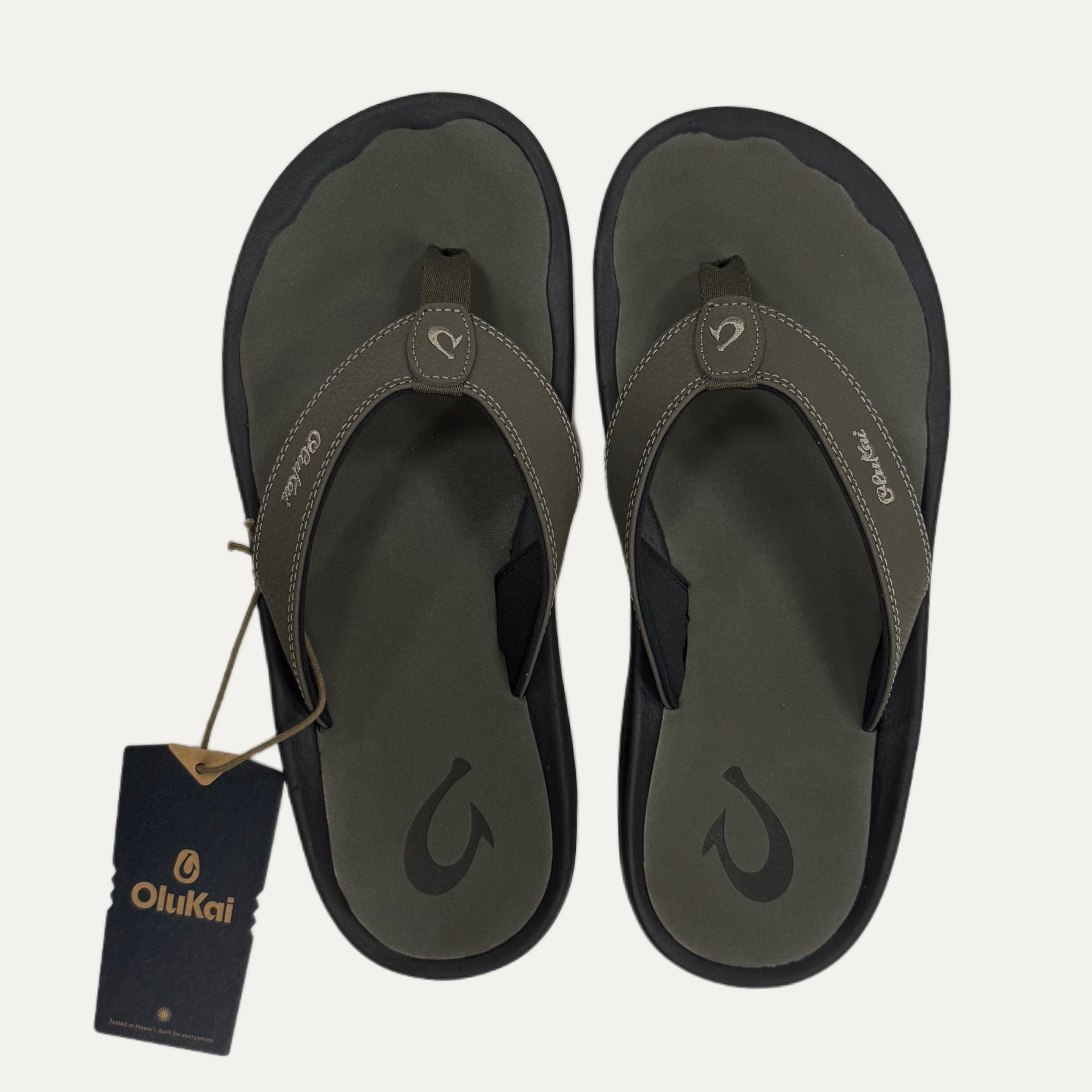 Pair of olive green flip flops with a tag on a white background