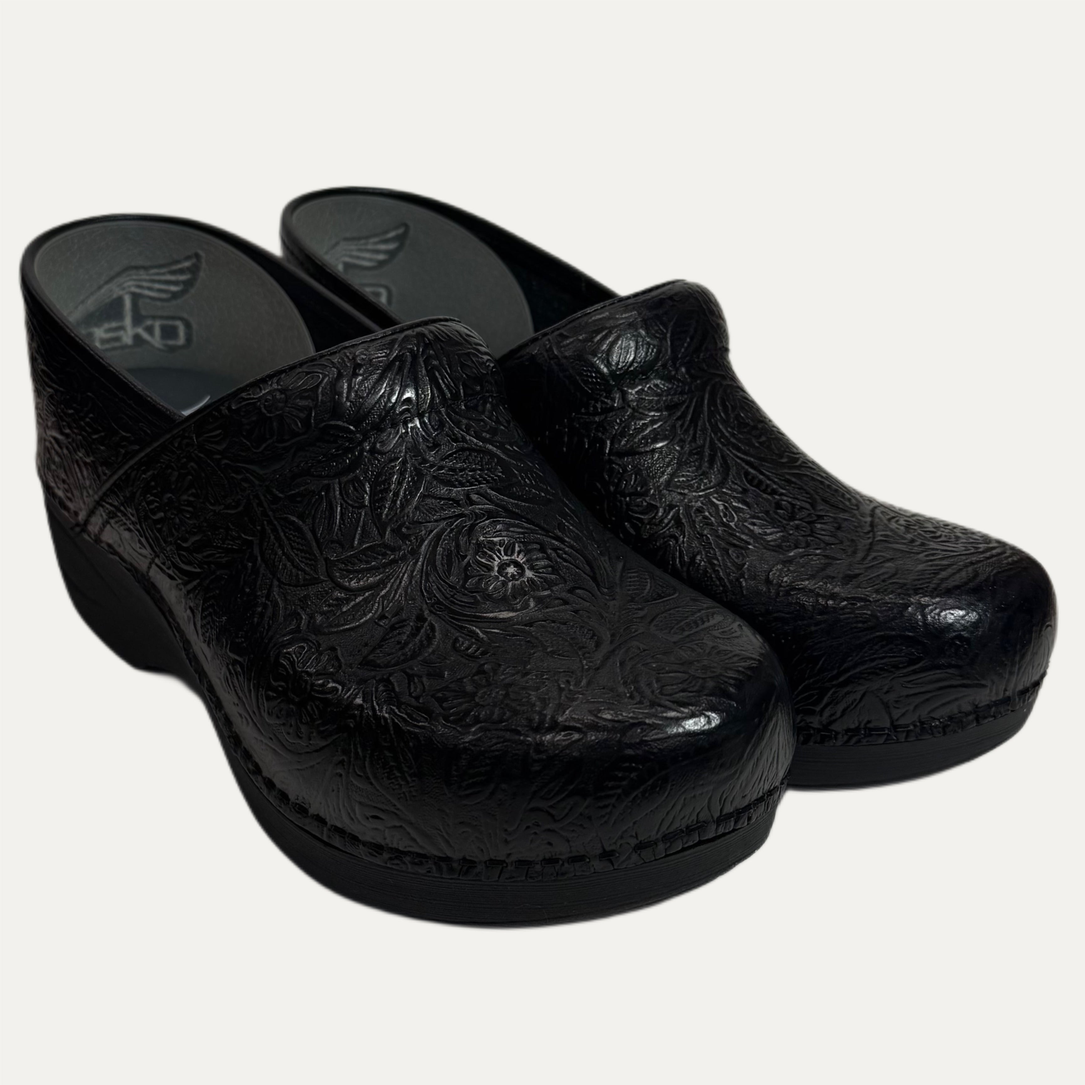 Pair of black leather clogs with embossed intricate designs on a white background