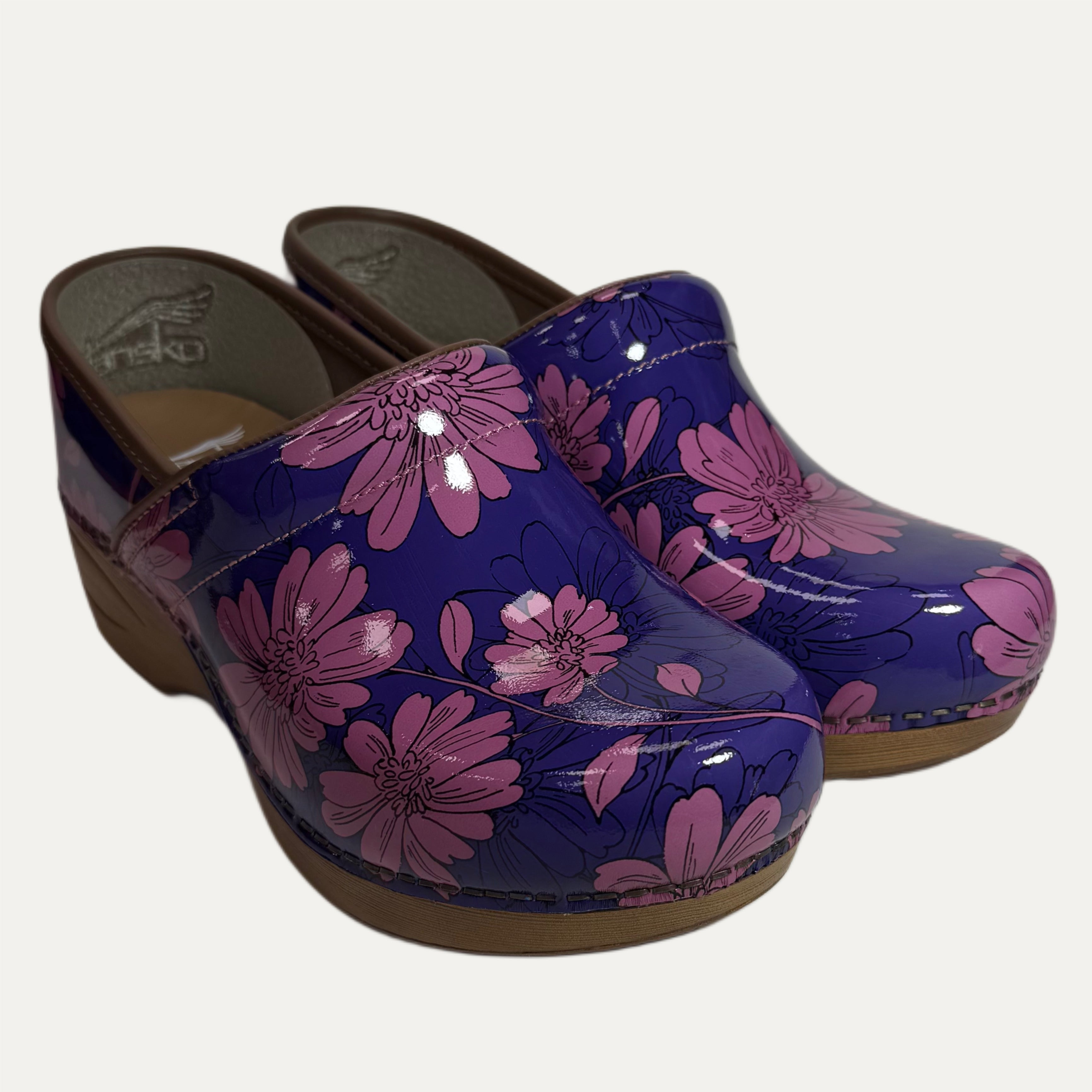 Pair of purple patent leather clogs with pink floral pattern on a white background